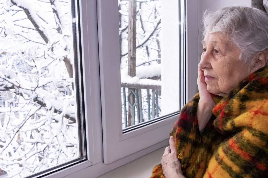 Elderly Woman looking out window with hand on face