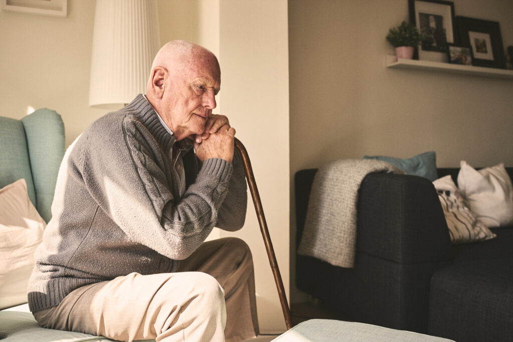 Elderly man with cane sitting in living room